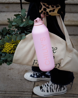 Pink water bottle with 'CHILLYS' branding held by a person wearing black and white sneakers.