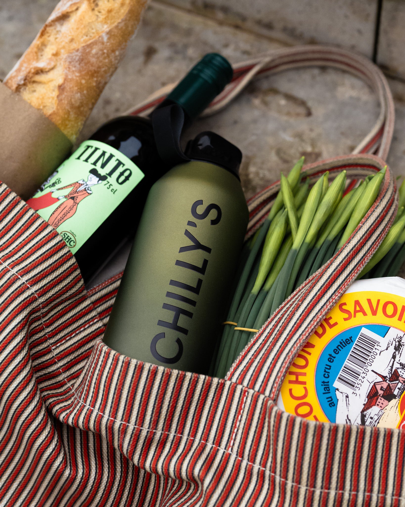 Bag with Chilly's bottle, green onions, and other items on a stone surface